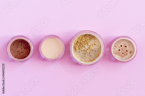 Mineral beauty makeup kit, foundation, bronzer, concealer, highlighter on pink colored background. Flat lay