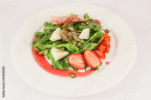 Mix of hot sausages with bacon on a cushion of lettuce leaves, in a duet with parmesan and strawberries, garnished with pumpkin seeds, dressed with raspberry sauce