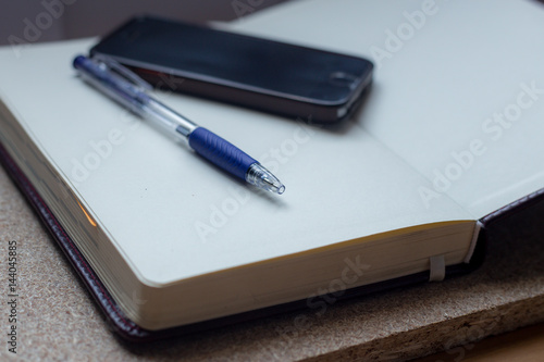 Empty notebook, mobile phone and a pen on wooden table