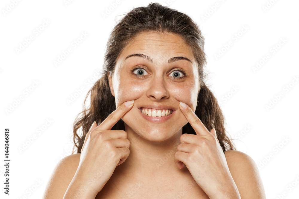 beautiful young woman with no makeup forcing her smile with her fingers beautiful young woman with no makeup forcing her smile with her fingers