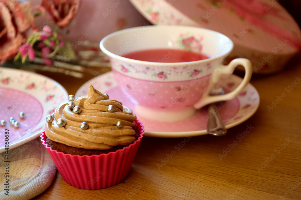 Pink chocolate cupcake frosted with chocolate butter-cream, pink teacup and plate, roses and pink gift box, afternoon tea Pink chocolate cupcake frosted with chocolate butter-cream, pink teacup and plate, roses and pink gift box, afternoon tea