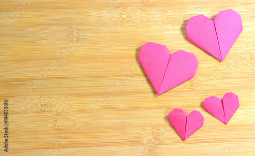 Pink origami hearts on a wooden background.