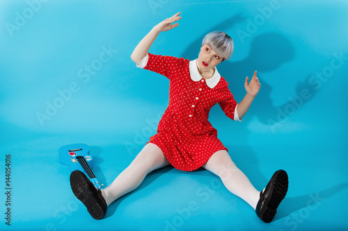 Picture of beautiful dollish girl with short light violet hair wearing red dress over blue background. photo