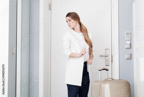 Pretty woman with suitcase in modern hotel room looking at mirror