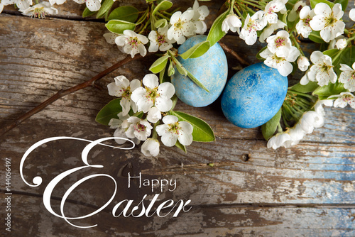 Happy Easter background with blue painted easter eggs, white flowers on wood background