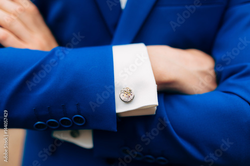 Crossed man's hands on his chest in a blue jacket. Cuff links from the watch mechanism. photo