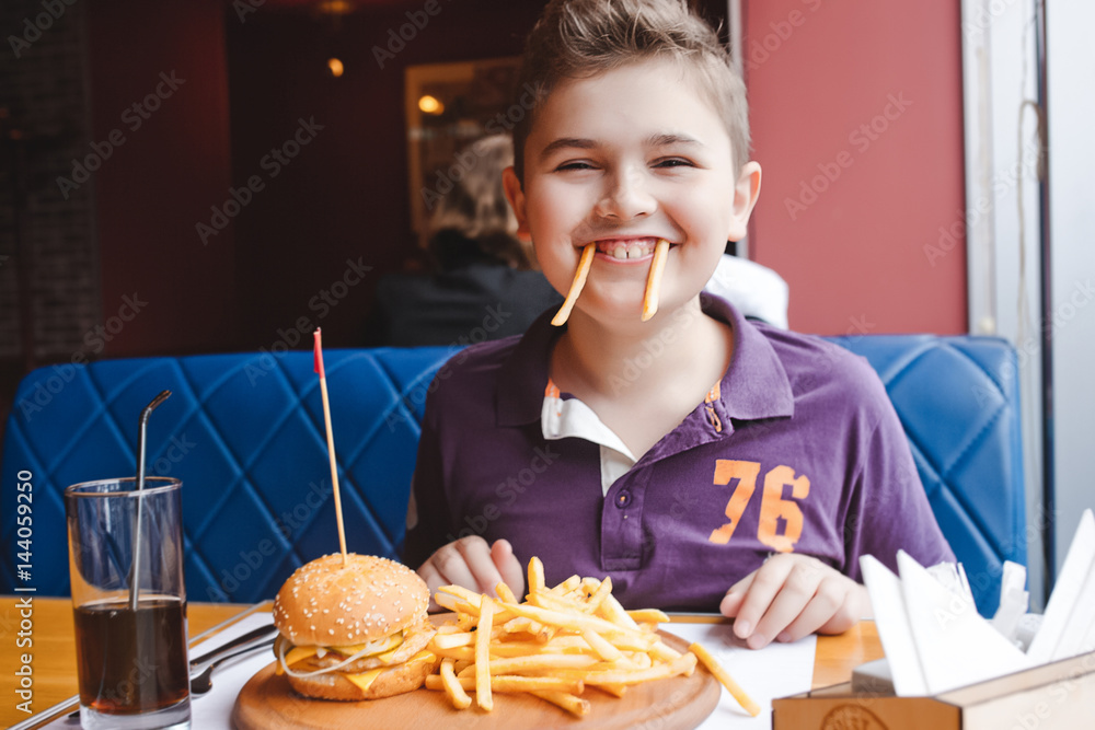 funny little boy eating a hamburger at a cafe, food concept