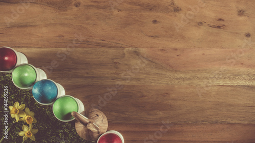 Easter eggs in eggcups with brown bunny in between on a brown wooden table with free text space