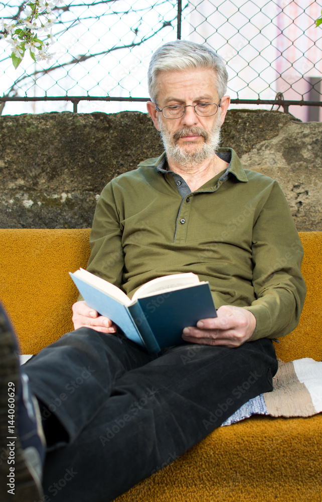 Senior man reading a book in sofa bed outdoors