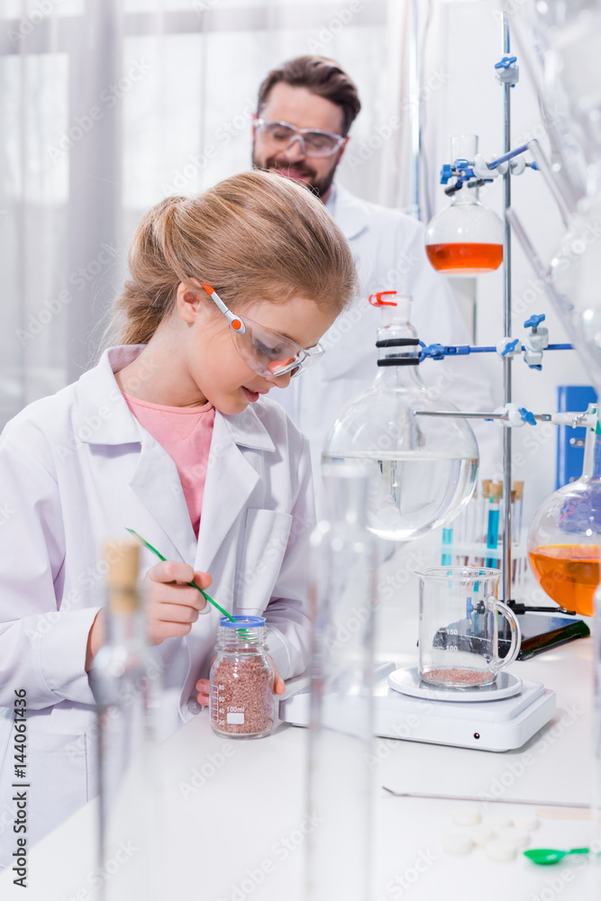 Smiling bearded teacher looking at little student making experiment in laboratory Smiling bearded teacher looking at little student making experiment in laboratory