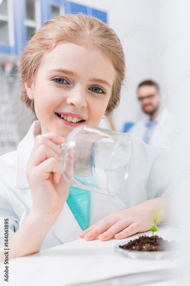 Smiling little girl in white coat working with green plant in laboratory Smiling little girl in white coat working with green plant in laboratory