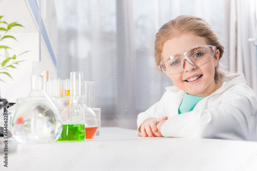 adorable little girl in goggles with flasks in laboratory looking at camera adorable little girl in goggles with flasks in laboratory looking at camera