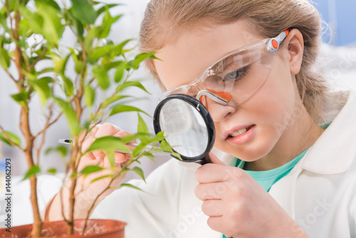 adorable little girl in goggles with magnifying glass and plant in laboratory
