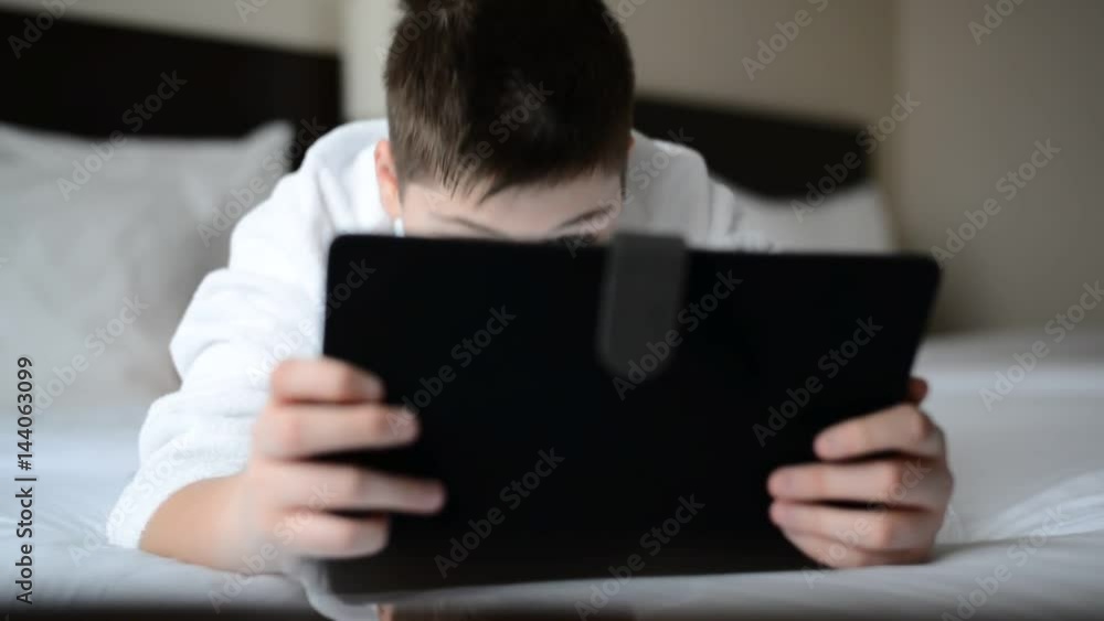 Teenager in white bathrobe on bed and playing on tablet Teenager in white bathrobe on bed and playing on tablet