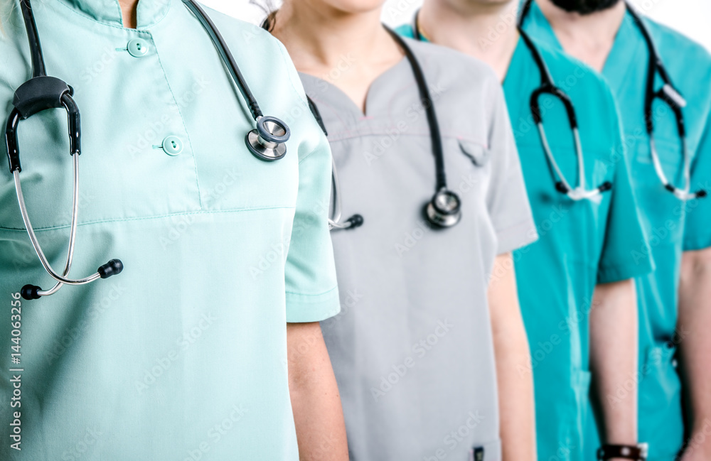 Doctors dressed in surgical suits stand in a row. On the necks of doctors hang black phonendoscopes. Doctors dressed in surgical suits stand in a row. On the necks of doctors hang black phonendoscopes.