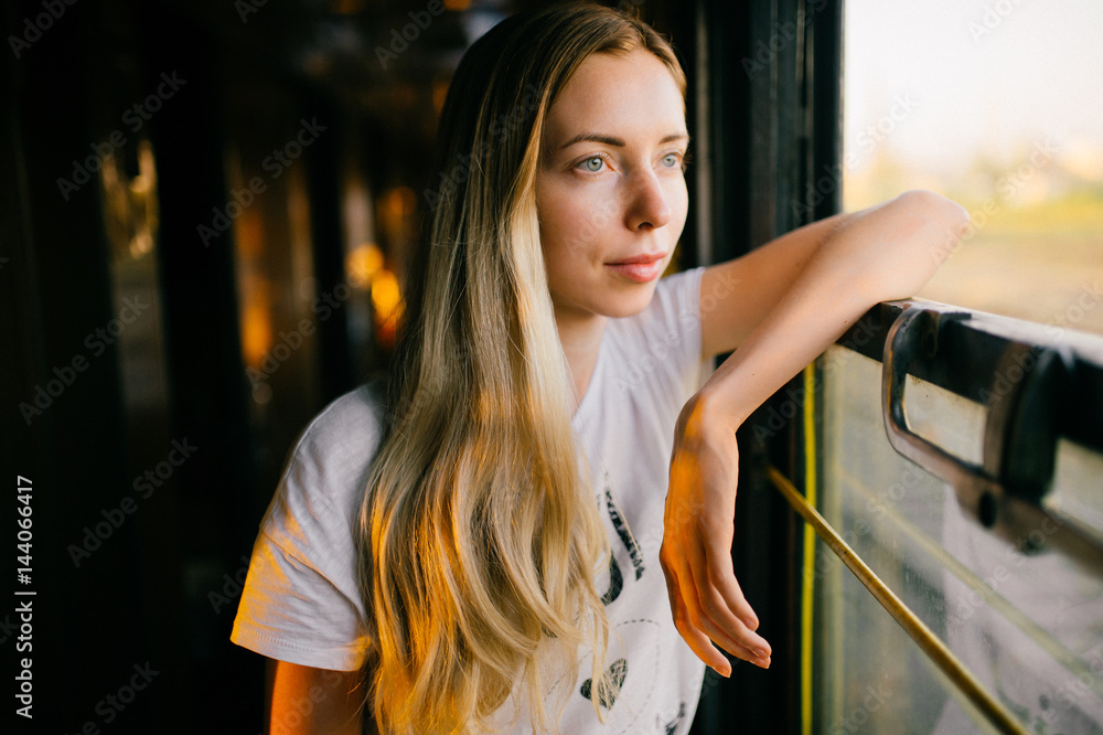 Photo of a very beautiful and attractive skinny teen girl with long hair in  sleeveless shirt traveling by train alone on vacation and looking at  window. Deep mood concept. Stock Photo