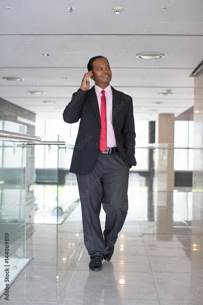 Smiling businessman walking in corridor with phone Smiling businessman walking in corridor with phone