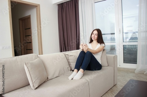 Happy girl reading a message in a smart phone sitting on a couch at home. Free Download Happy girl reading a message in a smart phone sitting on a couch at home. - GFXLoad