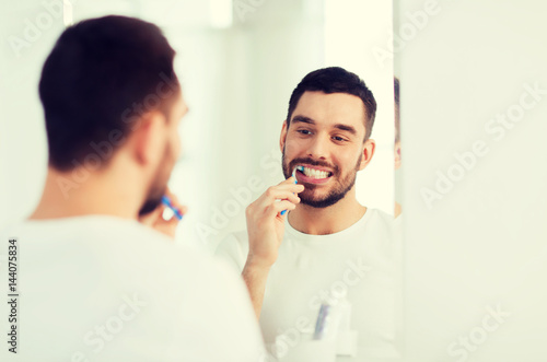 man with toothbrush cleaning teeth at bathroom