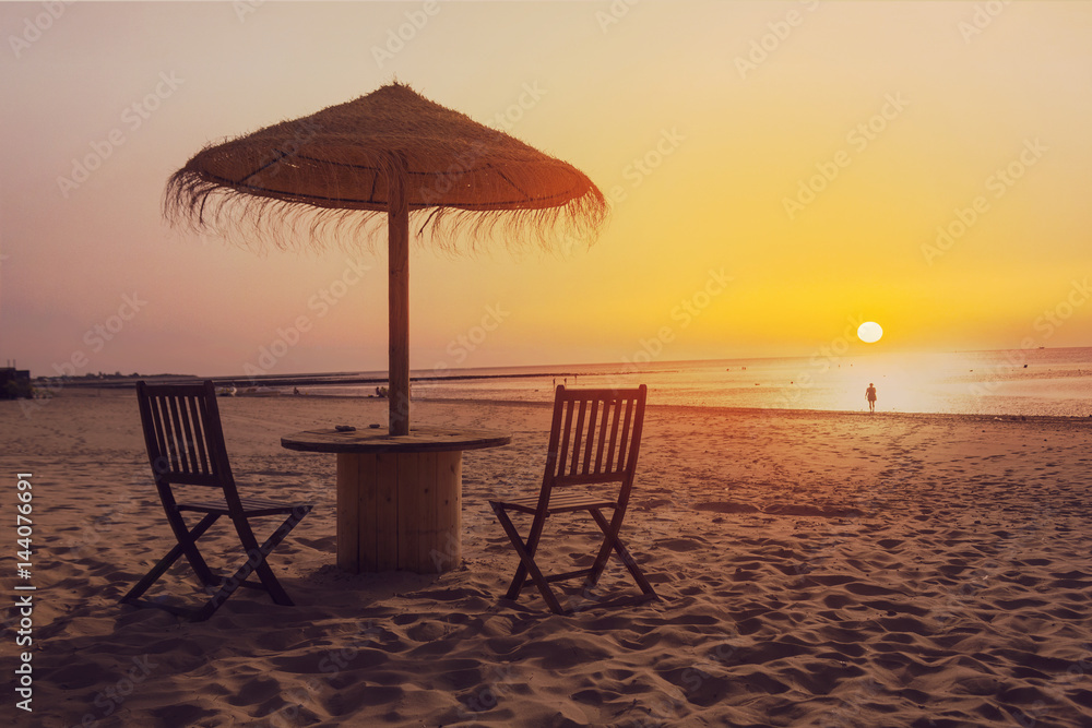 Wooden table and chairs with umbrella on the beach at sunset