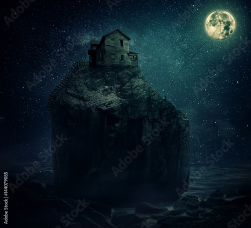 Surreal image with a wood house on the top of a rock hill, near the sea, beyond the starry night sky and a young man, holding a rope, try to catch and pull the full moon.