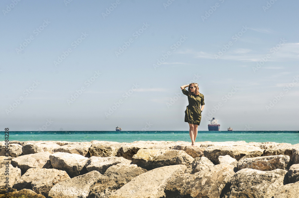 Beautiful young  woman standing on rocks border and looking forward on sea.