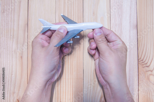 Man hand holding miniature of plastic airplane on wood table.