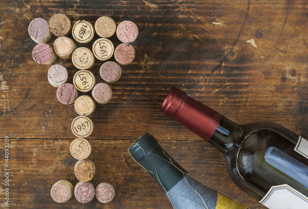 Two red wine bottle and  used wine corks in shape of wine glass on old vintage cutting board. 