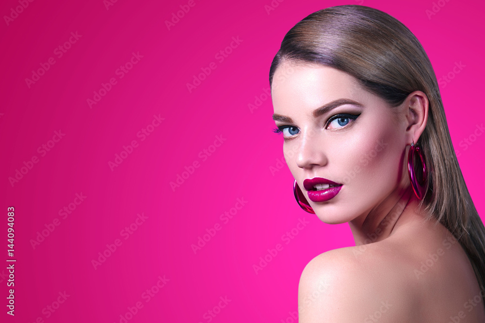 Fototapeta premium Beautiful fashionable girl with long smooth hair with large pink shiny earrings. Girl in the studio on a pink background. Cosmetics, hairdresser, beauty, fashion, spa, salon.
