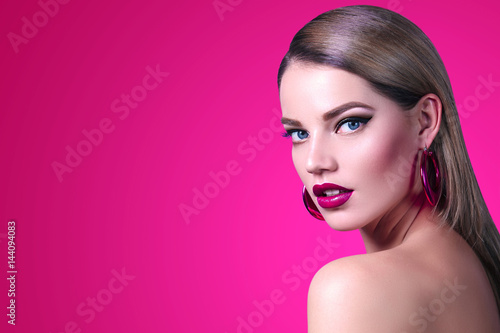 Beautiful fashionable girl with long smooth hair with large pink shiny earrings. Girl in the studio on a pink background. Cosmetics, hairdresser, beauty, fashion, spa, salon.