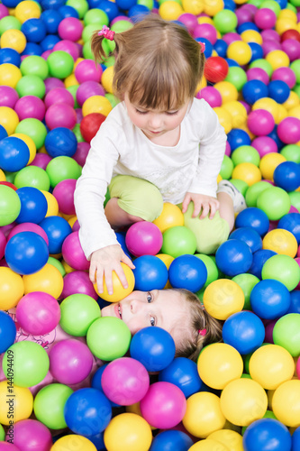 Two children play fun in colorful balls and one girl lays balls on another