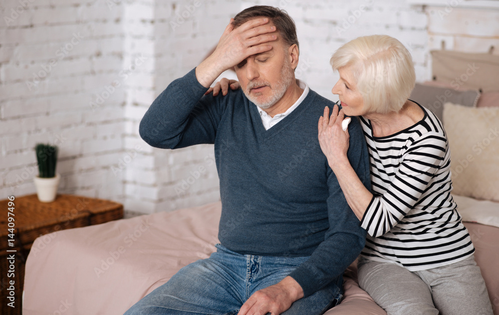Senior ill man sitting on bed near wife Senior ill man sitting on bed near wife