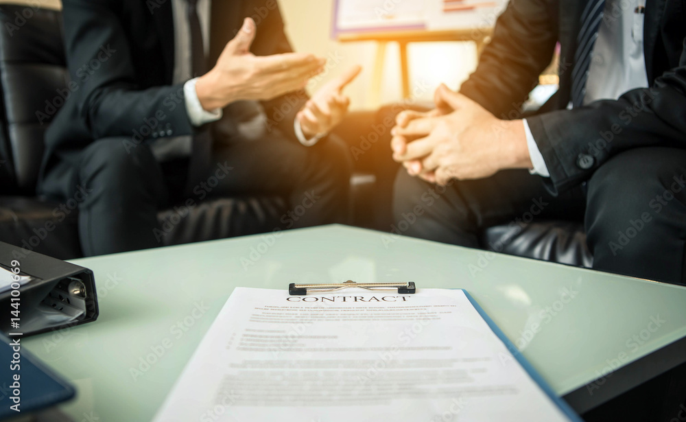 Close-up of business contract with pen at workplace on background of office workers interacting. Close-up of business contract with pen at workplace on background of office workers interacting.