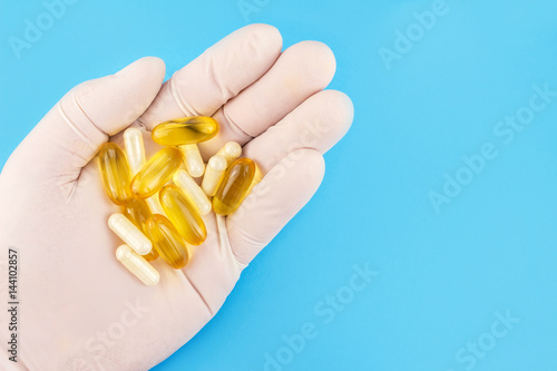 Hand in medical glove keeps lot of capsules, omega 3, fish oil and glucosamine on blue background.