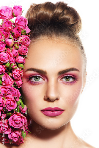 Young beautiful woman with hair bun and pink roses near her face over white background, copy space