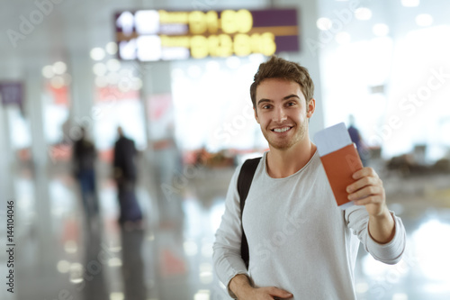 Handsome man with his luggage and travel documents walking at the airport
