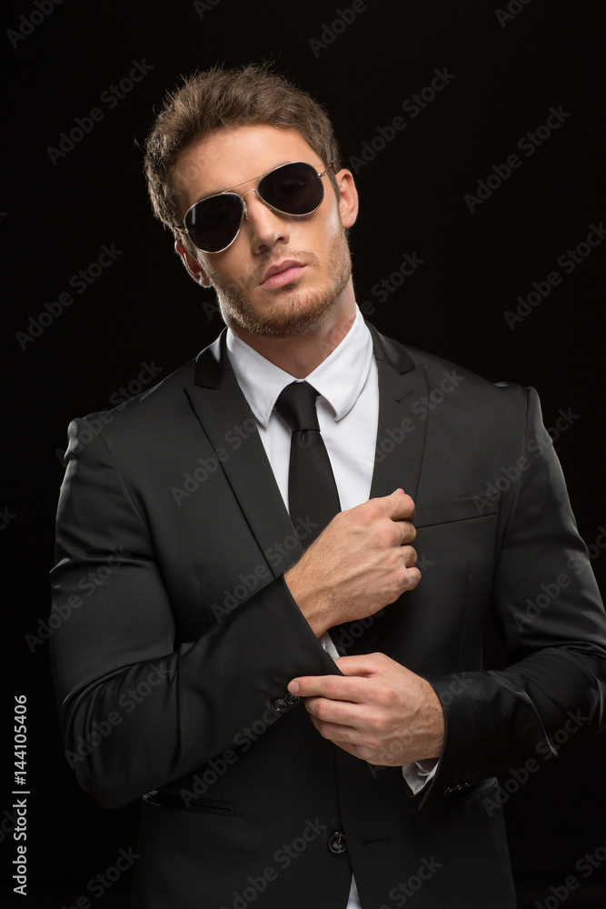 Handsome serious young man in a suit and sunglasses on black background ...