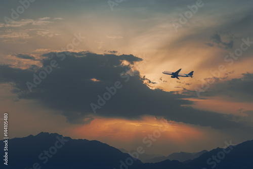 Silhouette of airplane above mountains at dawn