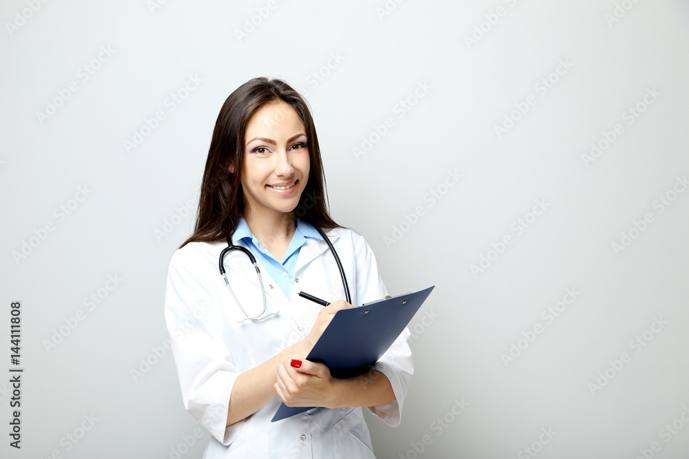 Portrait of young medical doctor with clipboard on a grey background Portrait of young medical doctor with clipboard on a grey background