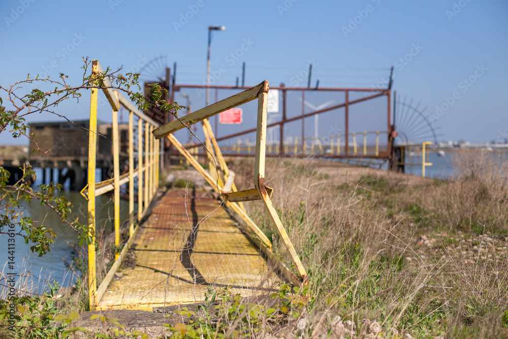 Damaged footbridge front of an abandoned rusted gate with razor wire on a seaside bridge at Isle of Sheppey England United-Kingdom Damaged footbridge front of an abandoned rusted gate with razor wire on a seaside bridge at Isle of Sheppey England United-Kingdom