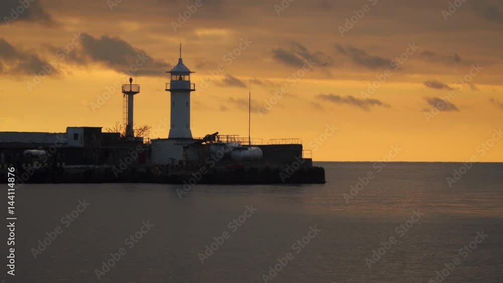 Breakwater with a lighthouse against the sky with clouds at sunset Breakwater with a lighthouse against the sky with clouds at sunset