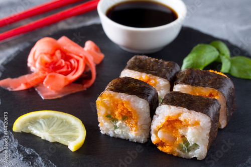 Roll Okinawa on a black slate board - tobiko orange caviar, shrimp, soft cheese, cucumber, nori, rice.