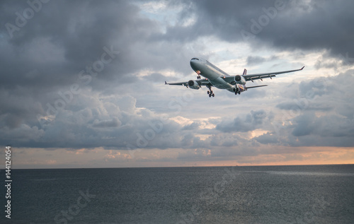 View from the beach on the landing airplane isolated above the sea over beautiful cloudy sky background