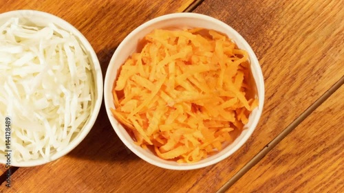 Chopped carrot and cabbage in white cup on wooden background close up. Ingredients for vegetable salad