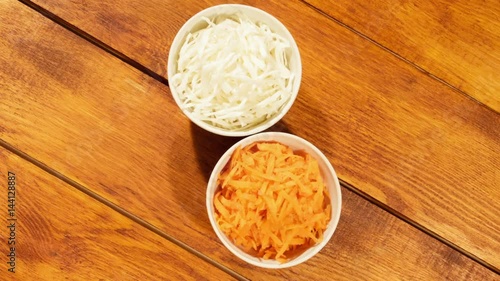 Chopped carrot and cabbage in white cup on wooden background close up. Ingredients for vegetable salad