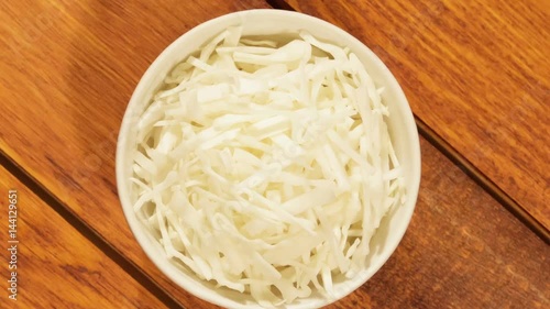 Chopped cabbage in white cup on wooden background close up. Ingredient for vegetable salad