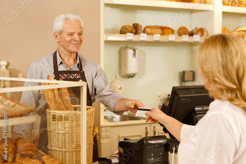 Senior professional baker taking a payment from his customer