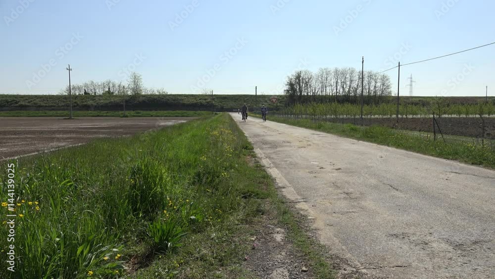 old cyclists slowly moving on dirt road in countryside