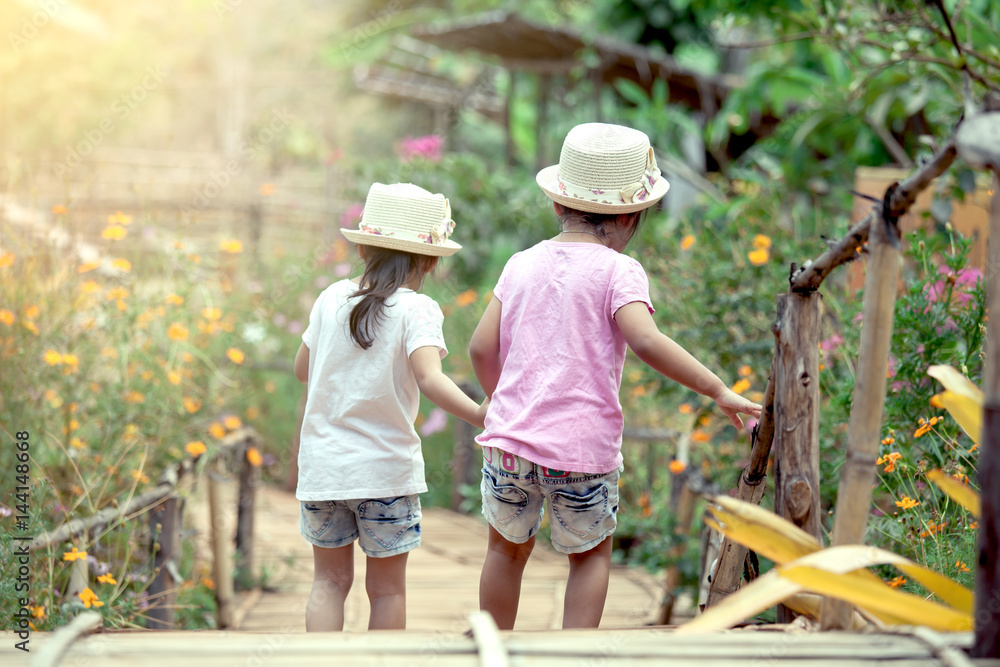 Back view of two little girls holding hand and walking together in the garden in vintage color tone
