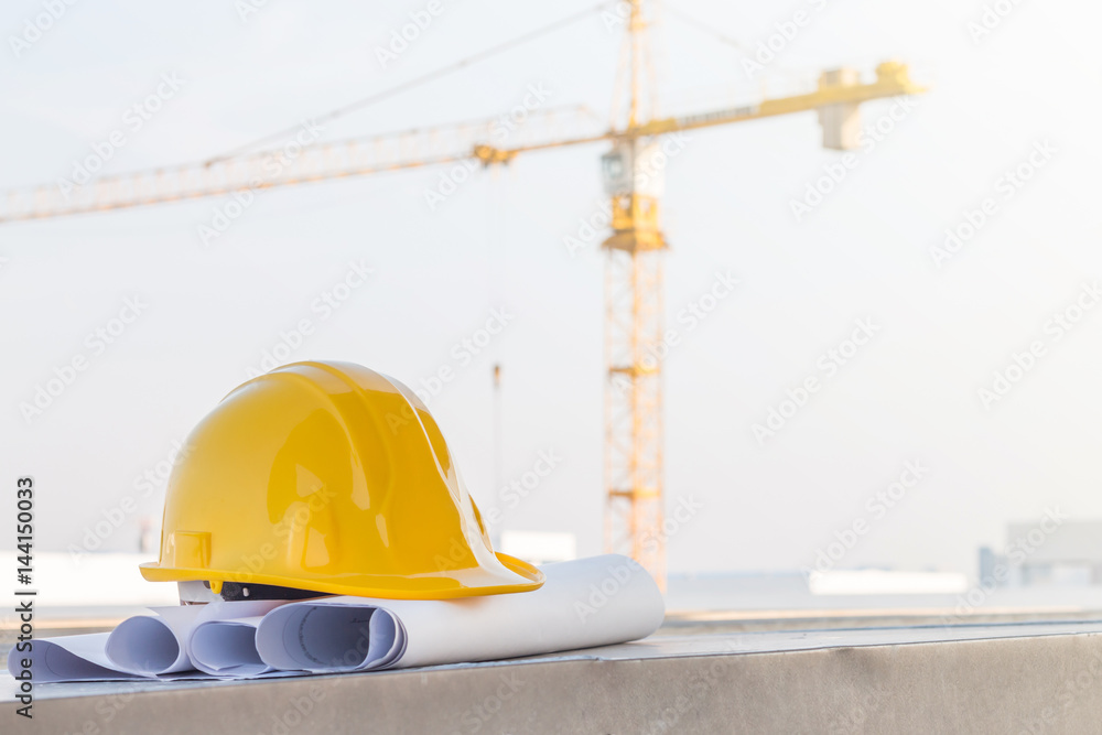 The yellow safety helmet put on the blueprint at construction site with crane background The yellow safety helmet put on the blueprint at construction site with crane background